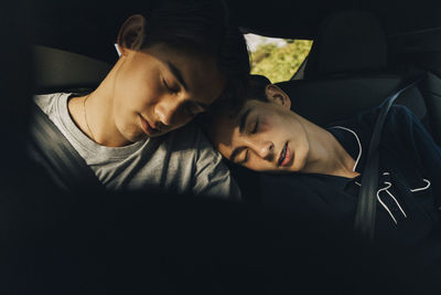 Teenage boy sleeping on brother's shoulder while sitting in car during road trip