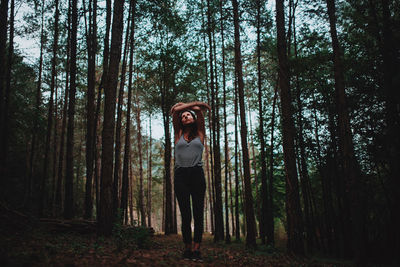 Full length of woman standing by trees in forest