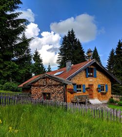 House on field by trees and houses against sky