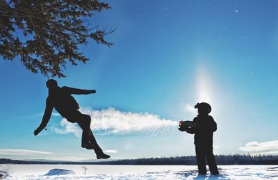 Friends playing with squirt gun on snowy field against sky