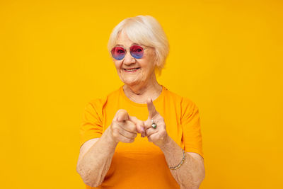 Portrait of young woman wearing sunglasses against yellow background