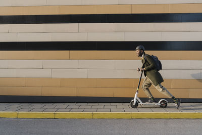 Stylish man with helmet and scooter passing a building