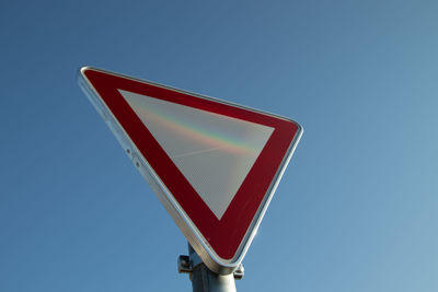 Low angle view of road sign against clear blue sky