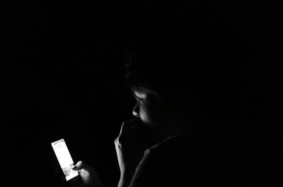 Side view of woman using mobile phone against black background