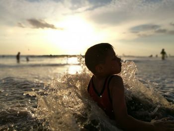 Close-up of boy in sea against sky during sunset