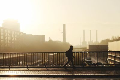Rear view of silhouette man walking on bridge against sky