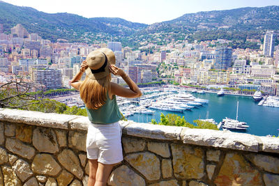 Beautiful stylish girl enjoying view of monte-carlo cityscape with skyscrapers and yachts