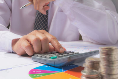 Midsection of businessman with coins on desk in office