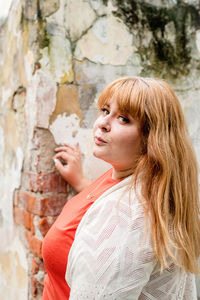 Portrait of young woman standing by wall outdoors