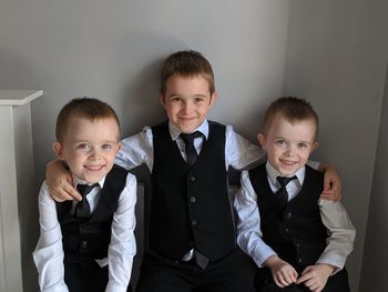 Portrait of smiling brothers wearing suits against wall at home