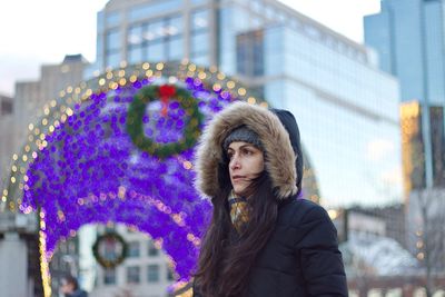 Young woman in warm clothing looking away while standing in city