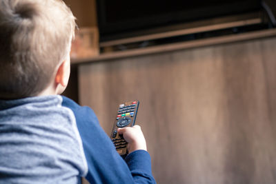 Rear view of boy with remote in hand at home