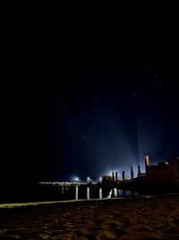 Illuminated buildings by sea against sky at night