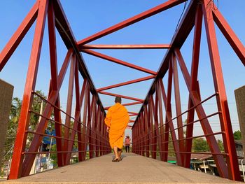 Rear view of monk walking on footbridge against sky