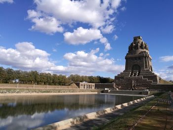 View of temple by lake against cloudy sky