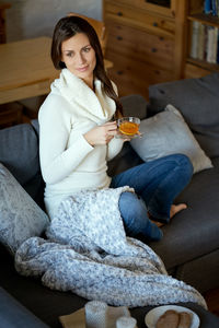 Full length of woman drinking tea while sitting on sofa at home