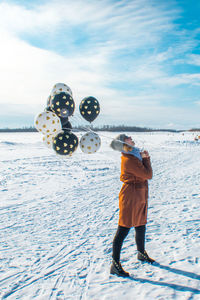 Woman with balloons standing on snow against sky