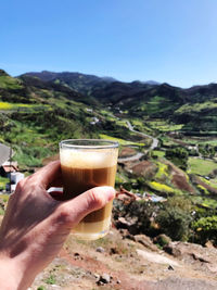 Close-up of hand holding drink against mountains