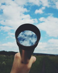 Close-up of hand holding camera against sky