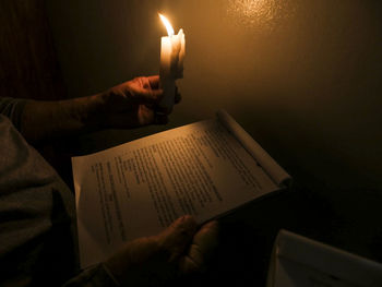 Midsection of person holding book and illuminated candle in darkroom