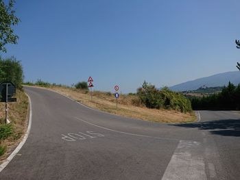 Road sign by trees against clear blue sky