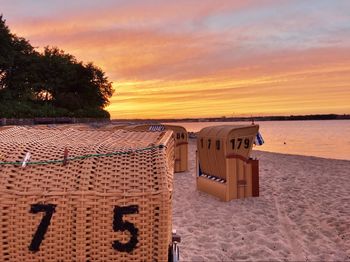 Hooded chairs on beach against sky during sunset