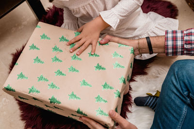 Cropped unrecognizable child opening present box between anonymous father during new year holiday at home