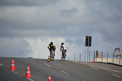 Rear view of friends riding bicycles on road against cloudy sky