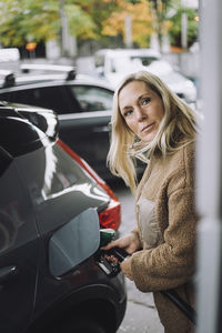 Mature woman with blond hair pumping gas in car at station