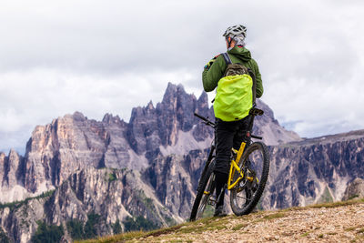 Rear view of person with bicycle on mountain against cloudy sky
