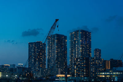 Illuminated modern buildings against blue sky at dusk