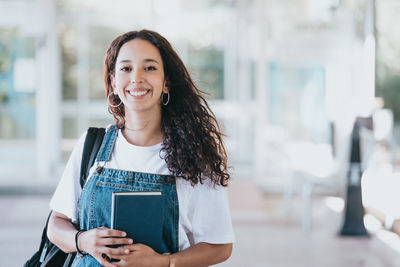 Portrait of young woman standing against building