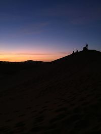 Silhouette people on desert against sky during sunset