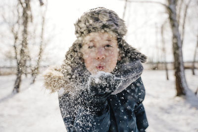 Boy blowing snow from palm in winter