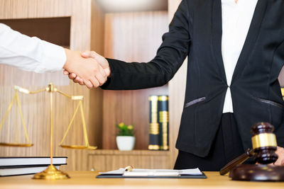 Midsection of lawyer handshaking with client in office