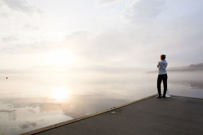 Woman standing on jetty and looking at sunrise