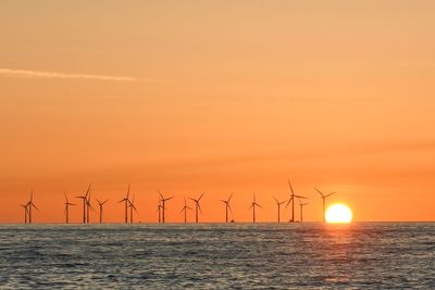 Wind turbines in sea against sky during sunset