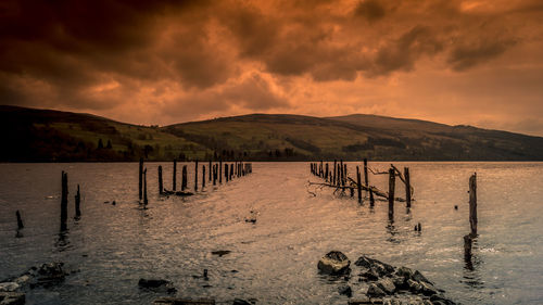 Wooden posts in lake against sky