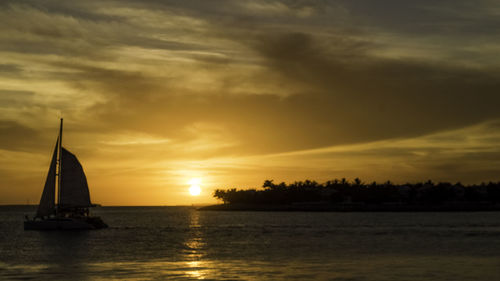 Sailboat sailing on sea against dramatic sky during sunset