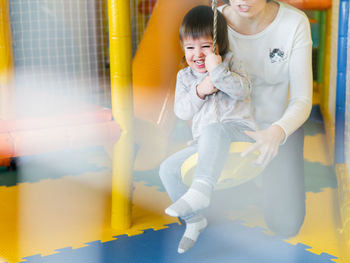 Toddler plays on rope swing with his mother or babysitter. physical development for little children.