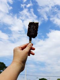 Person holding ice cream cone against sky