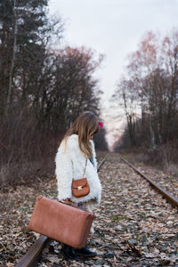 Girl holding suitcase while standing on railroad track