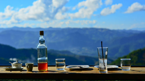 Bottles on table by mountains against sky