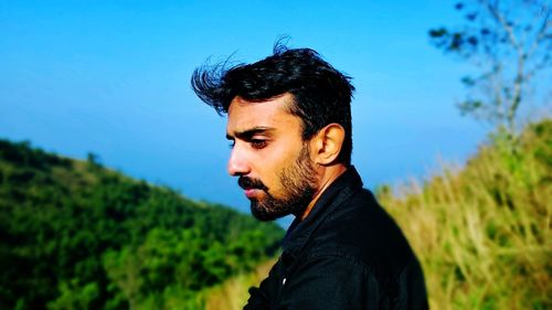 Portrait of young man looking away against blue sky