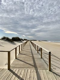 Wooden pier on beach against sky