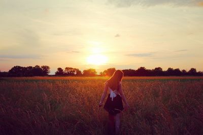 Rear view of man standing on field against sky during sunset