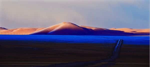 Scenic view of road amidst field against sky during sunset