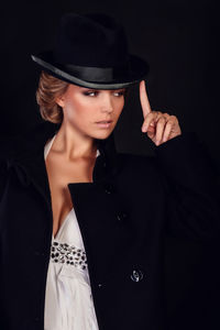 Portrait of woman wearing hat standing against black background