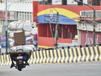 Rear view of person with luggage riding motor scooter on road