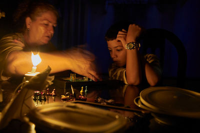 Grandmother playing chess with grandson on illuminated table in darkroom